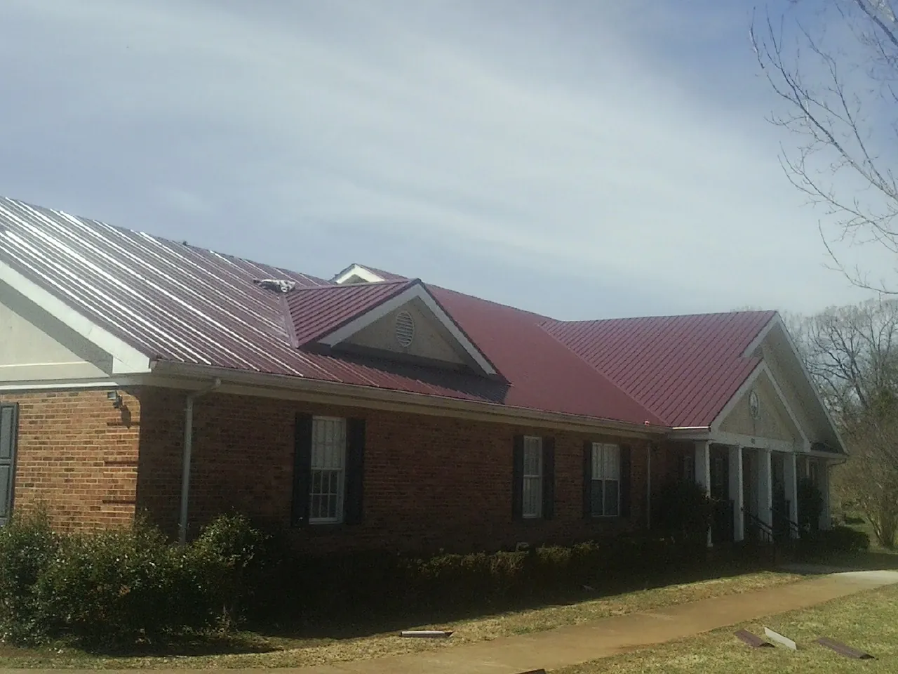 Red metal roof with gabled entries on a long brick building, from a Hail Damage Roof Repair job in Jacksontown