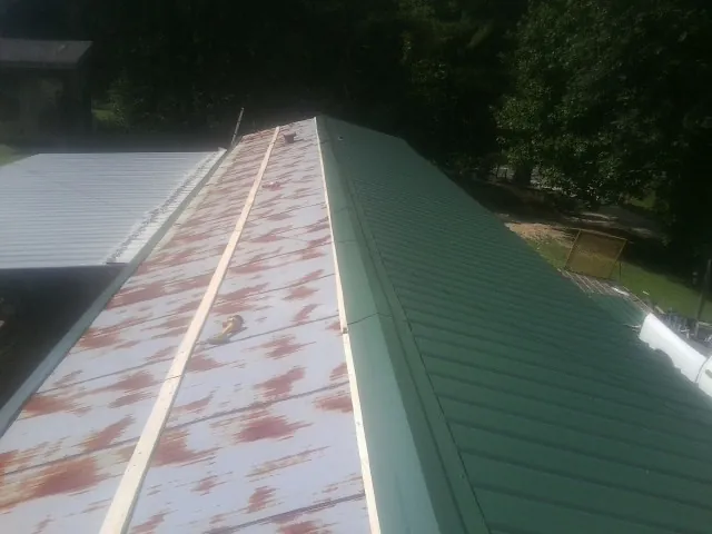 Old rusted panels beside newly installed green metal roofing — Wind Damage Roof Repair by Roofing Brothers in Jacksontown