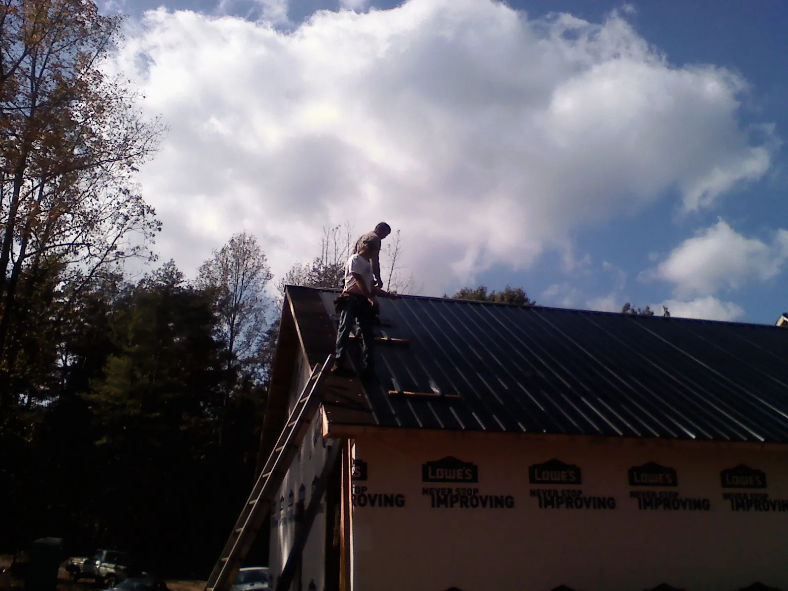 Roofer fastening dark metal panels high against a cloudy sky, from a Roof Inspection job in Jacksontown